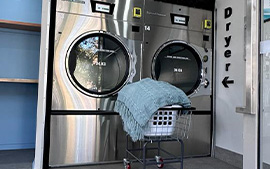 Two extra large touch screen cashless stainless steel 34 kg dryers. There is a trolley containing dried green blanket