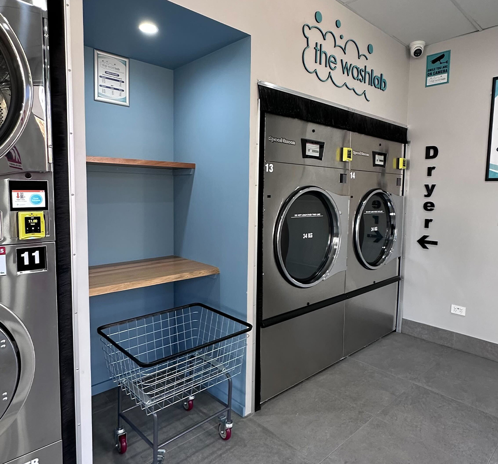 Interior of a Wash Lab laundromat showing a stainless steel 34 kg dryer and a clothes trolley